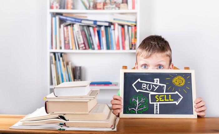 A child holds draws "buy" and "sell" arrows on a small blackboard.